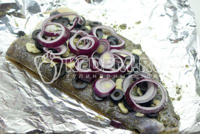 Рыбу натрите солью и поперчите по вкусу. Выложите на смазанную маслом фольгу, поверх положите порезанный полукольцами лук, порезанные кружочками зубчики чеснока и маслины